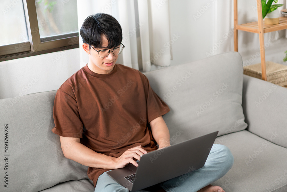 Technology Concept The man that is putting on glasses leaning his back on the dark yellow while focusing on the laptop’s screen. Technology Concept The man that is putting on glasses leaning his back on the dark yellow while focusing on the laptop’s screen.