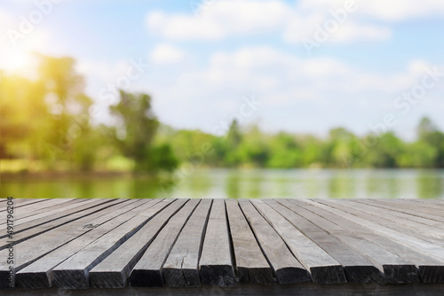 Empty old wooden table in front of blurred background of the lake, mountain, big tree and blue sky among bright sunlight on a clear day. Can be used for display or montage for show your products.