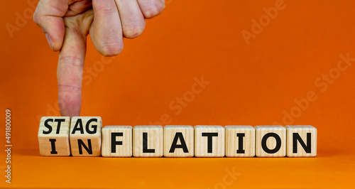 Stagflation or inflation symbol. Businessman turns cubes and changes the concept word inflation to stagflation. Beautiful orange background, copy space. Business stagflation or inflation concept. photo