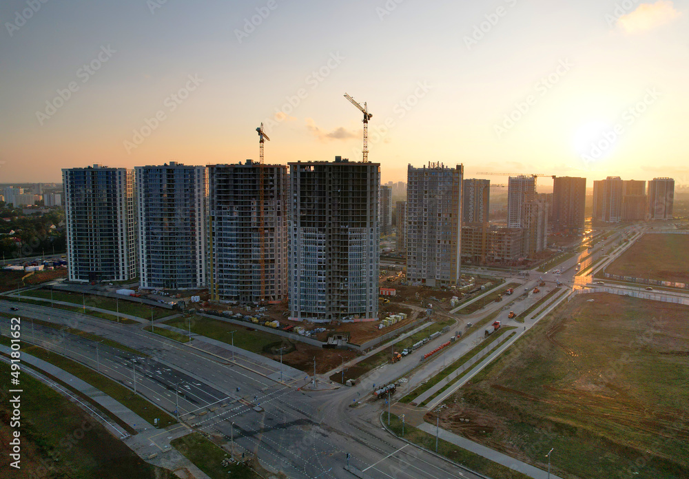 Crane during the construction of a residential building at sunset. Construction site at sunset with a tower crane and unfinished buildings and residential houses skyscrapers.