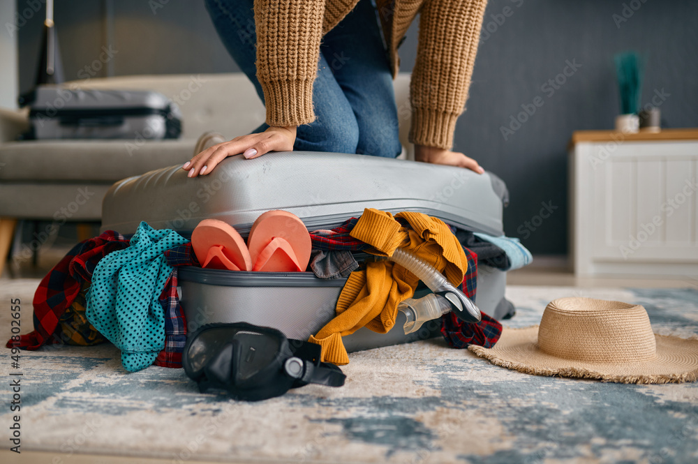 Woman trying to close overload travel suitcase