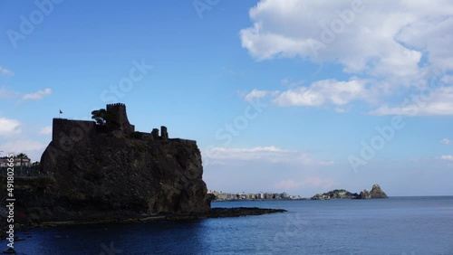 Time Lapse di un paesaggio marittimo, con le nuvole che scorrono veloci sul castello e i faraglioni di Aci Trezza in Sicilia photo
