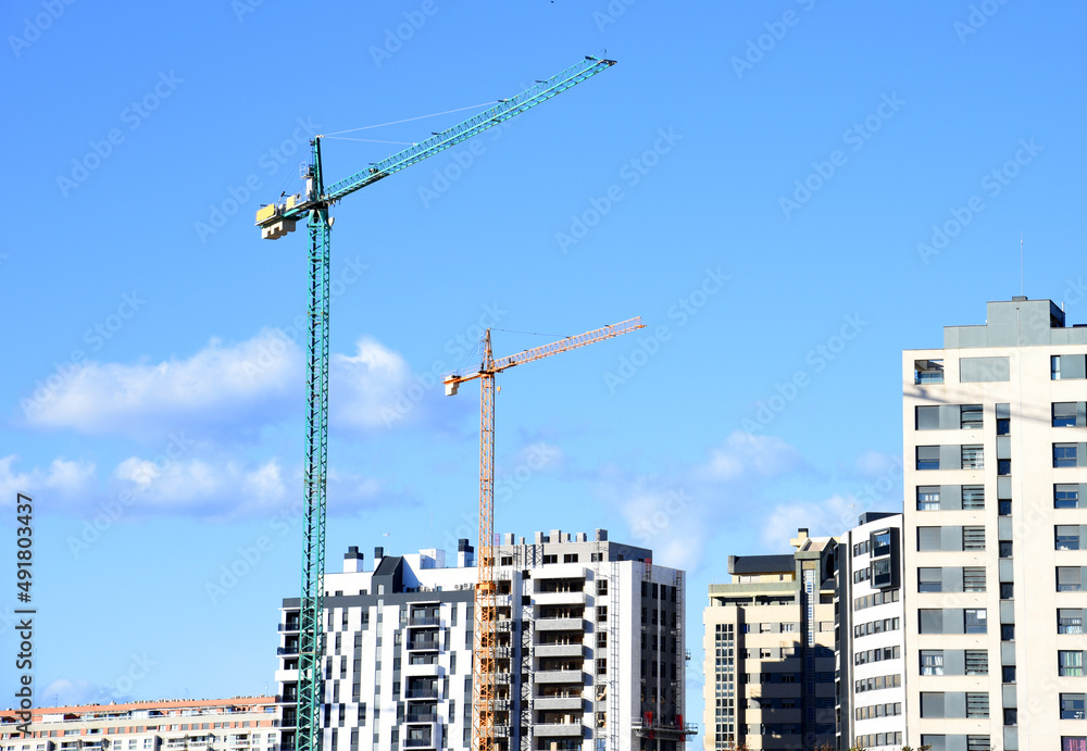 Tower crane against the blue sky. Tower crane on the construction of a residential building in Spain. Construction site with cranes for building construction. Сranes in action. Housing renovation 