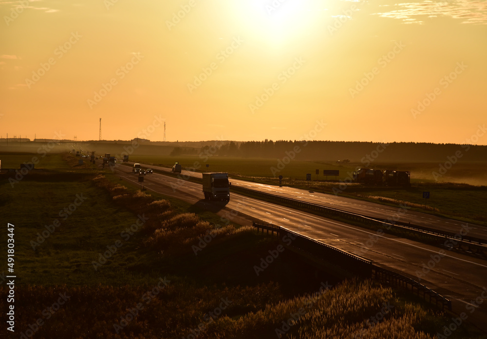 Fototapeta premium Trucks with Semi-trailer driving on highway on sunset. Goods Delivery. Services and Transport logistics. Lorry driven on highway. Traffic on road. Semi truck in motion drive. Semi-trailer truck..