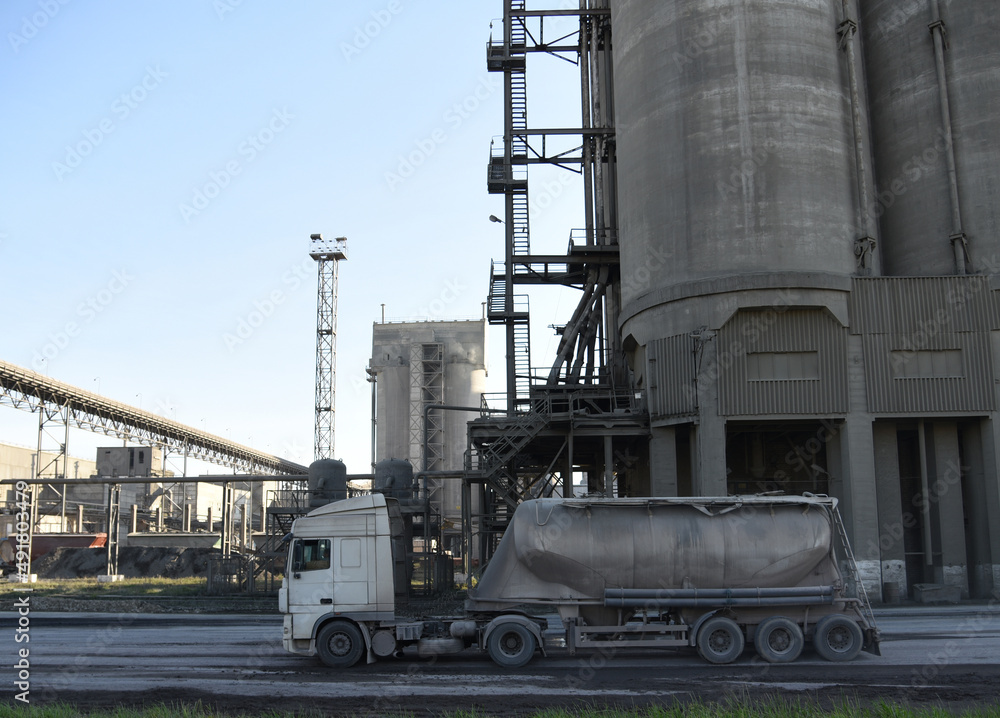 Obraz premium Truck with cement semi-trailer at cement plant site. Сement mix production at industrial factory. Industrial plant for the production of dry construction mixes. Concrete-mixing plant. Dry mix mortar.