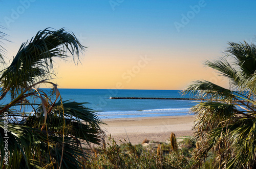 Empty beach on the sea with palm trees. Stone pier on coastline from to side Playa Puebla de Farnals. Coast at sea with waves on sunset sky background. Sea and palms at coastline in Spain. .