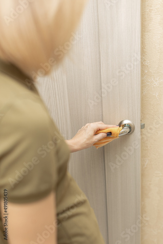 woman wipes the handle of an interior door with a rag