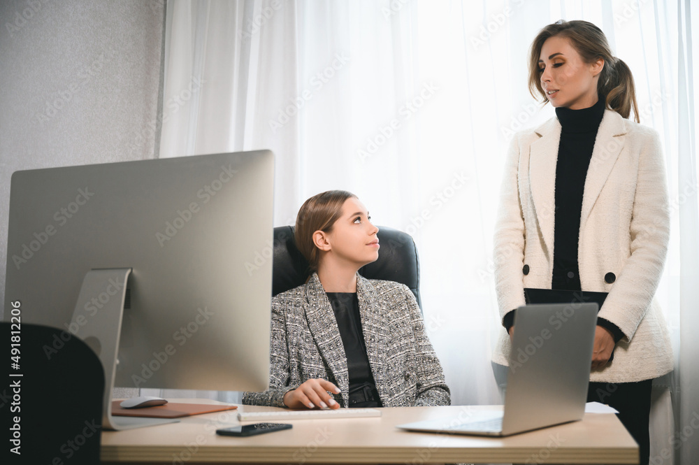 Attractive young adult women work together in the office at a meeting. A new employee consults with a mentor and presents a new project. Open space concept for teamwork Attractive young adult women work together in the office at a meeting. A new employee consults with a mentor and presents a new project. Open space concept for teamwork