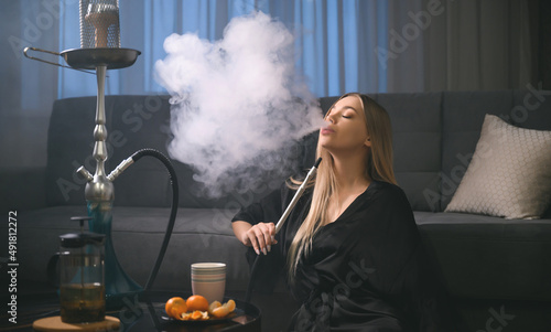 An attractive young adult woman smokes a hookah at home in anticipation of a party with her friends