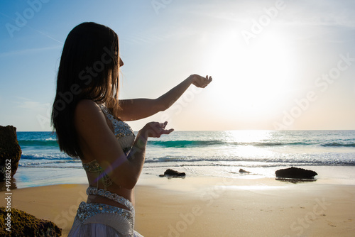 Happy and calm woman poses on the beach wearing the typical belly dance costume. Exotic beauty. Girl silhouette.