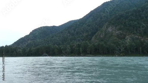 Wild mountain river.View from bank. Motor boat in water. Fast stream, hills and forest behind. Cloudy day. Altai Republick, Russia. High quality 4k footage