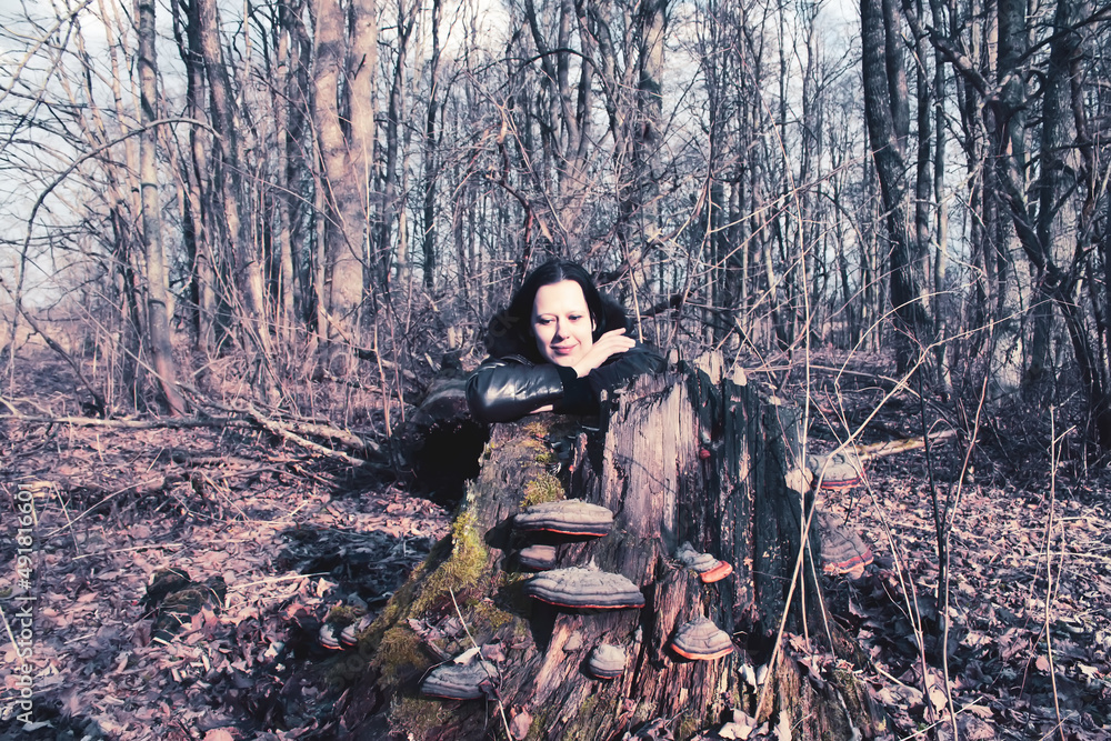 A young woman hides behind a large tree stump in the forest.