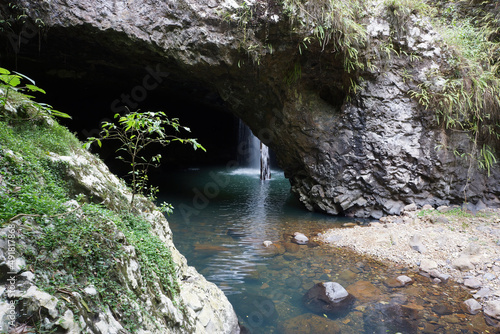 Natural Bridge also known as Natural Arch with water cascading over a fallen log into the water below in the Springbrook National Park, Queensland, Australia.