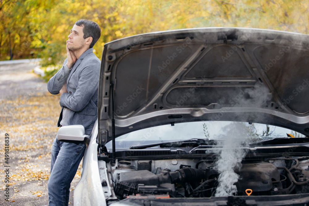 Foto de A man looks under the open hood of a car. The car broke down on