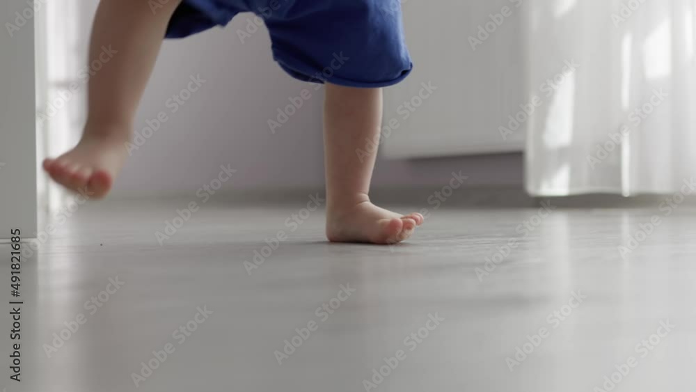 unrecognizable baby toddler doing first steps barefoot legs in blue pants on grey floor room indoors. child learning to walk. tiny toes feet fingers close-up. development skills, physical education unrecognizable baby toddler doing first steps barefoot legs in blue pants on grey floor room indoors. child learning to walk. tiny toes feet fingers close-up. development skills, physical education