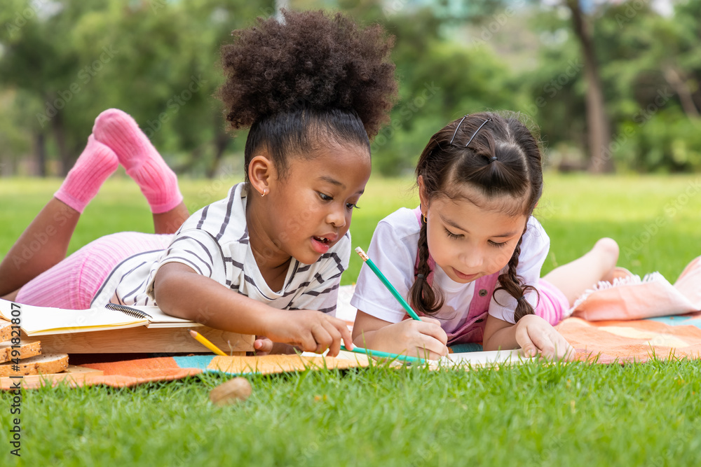 Two young girls multiracial lying and draw on lawn in the park on beautiful summer day, doing homework with friend. Two young girls multiracial lying and draw on lawn in the park on beautiful summer day, doing homework with friend.