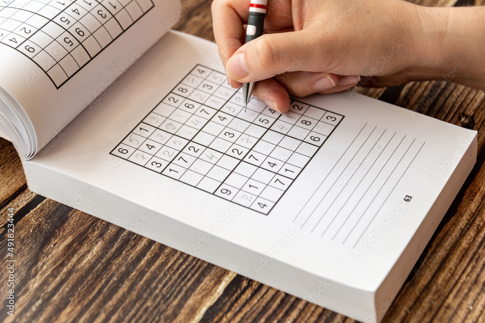 A person solving a sudoku puzzle on a wooden table A person solving a sudoku puzzle on a wooden table