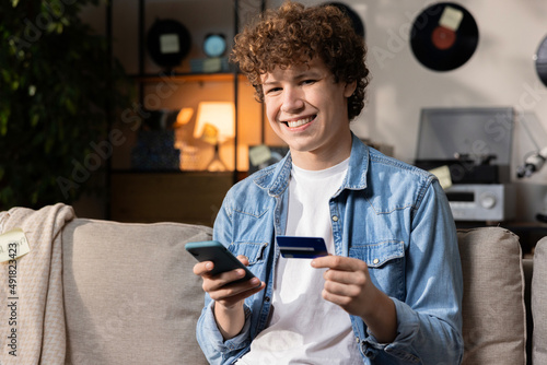 A smiling boy is sitting on a sofi, made a transfer online for a new English course. He wants to expand his knowledge by developing basic language skills. Internet transfer. photo