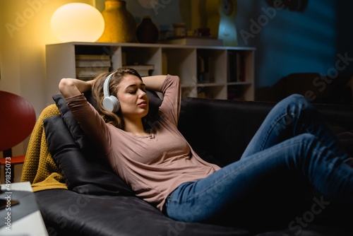 woman listening to a music and relaxing on sofa in her living room. night scene