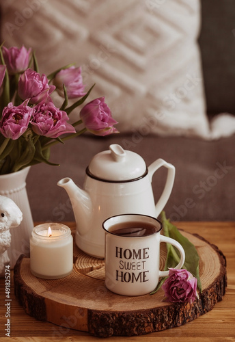 Still-life. A vase with flowers, tulips, a teapot, a bunny, a candle and a cup of tea on the coffee table in the living room home interior. Cozy spring concept.