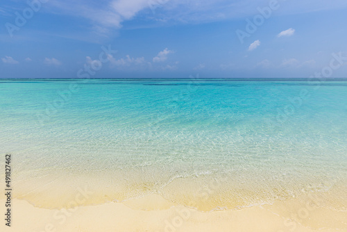 Closeup sandy beach waves and blue summer sky. Panoramic beach landscape. Empty tropical beach and seascape. Bright blue sky, soft sand, calmness, tranquil relaxing sunlight, summer mood