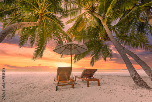 Tranquil tropical sunset scenery, two sun beds, loungers, umbrella under palm tree. White sand, sea view with horizon, colorful twilight sky. Calm relax beach resort hotel. Honeymoon, vacation travel