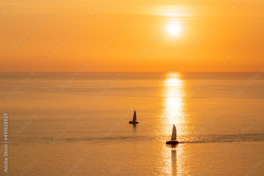 Beautiful gold and orange sunset with sailboat sailing through reflection of sunlight