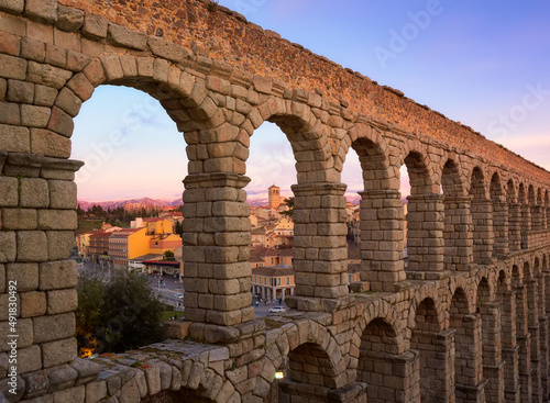 Parte del acueducto Romano de Segovia,Castilla y León, España  y sus arcos, a través de los que pueden observarse las montañas nevadas de la ciudad de Segovia y su arquitectura, al atardecer