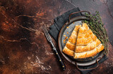 Slices of baked Round Borek cheese pie in kitchen tray with herbs. Dark background. Top view. Copy space