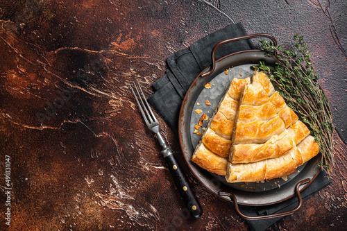 Slices of baked Round Borek cheese pie in kitchen tray with herbs. Dark background. Top view. Copy space photo