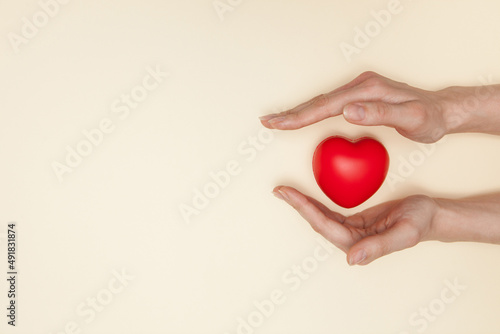 Health, medicine and charity concept - close up of female hands with small red heart. Flat lay.