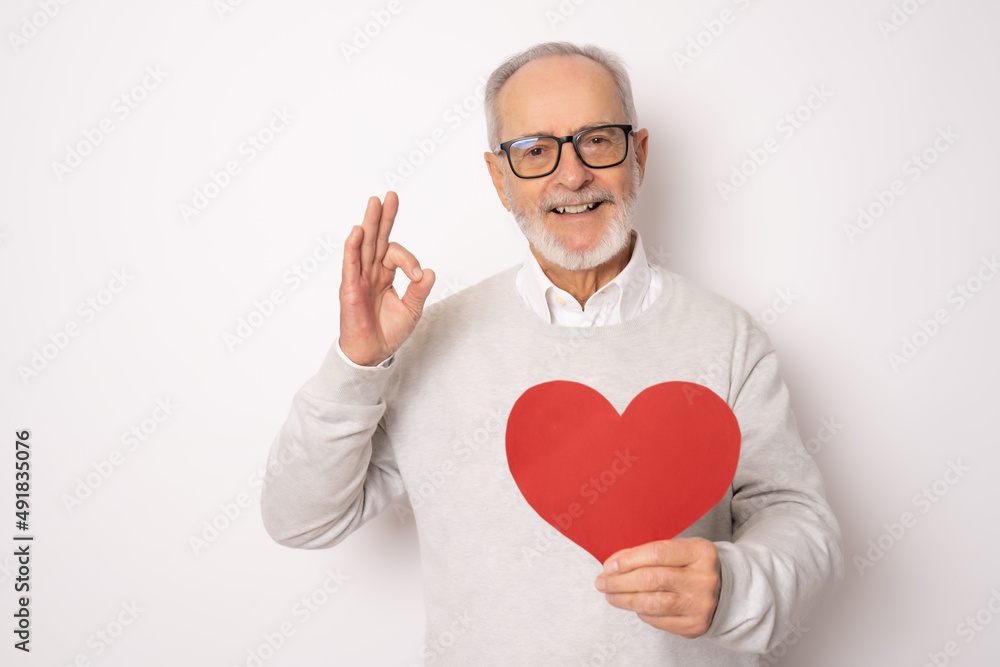 Happy senior man showing red paper heart and with okay sign isolated over white background. Health concept. Happy senior man showing red paper heart and with okay sign isolated over white background. Health concept.