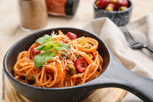 Frying pan with delicious Pasta Puttanesca on table, closeup