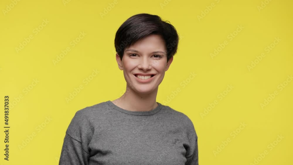 Portrait of young smiling beautiful woman wearing gray sweatshirt isolated on yellow background Portrait of young smiling beautiful woman wearing gray sweatshirt isolated on yellow background