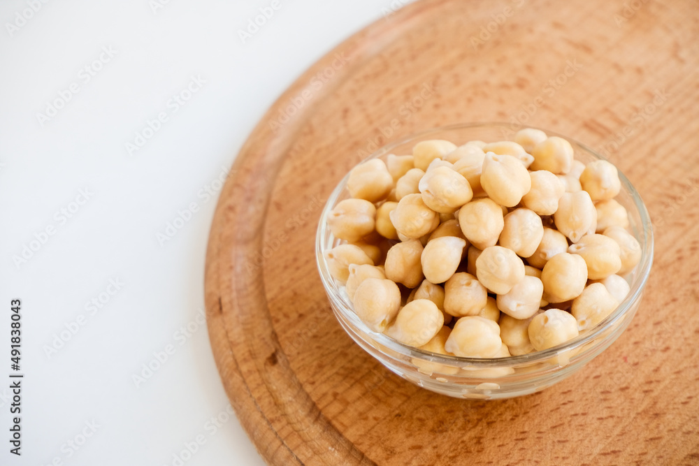Fresh raw organic chickpeas soaked in water on a white table on a wooden tray. The benefits of legumes. Vegan nutritive proteinaceous food. Taking care of your health. Ingredient of healthy vegan food