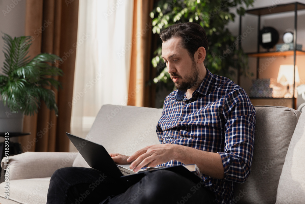 A young man with a beard works remotely from his living room couch. The political crisis has made it necessary to work from home. A young man with a beard works remotely from his living room couch. The political crisis has made it necessary to work from home.