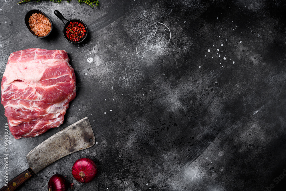 Piece of fresh raw pork from the neck, with ingredients and herbs , with old butcher cleaver knife, on black dark stone table background, top view flat lay, with copy space for text