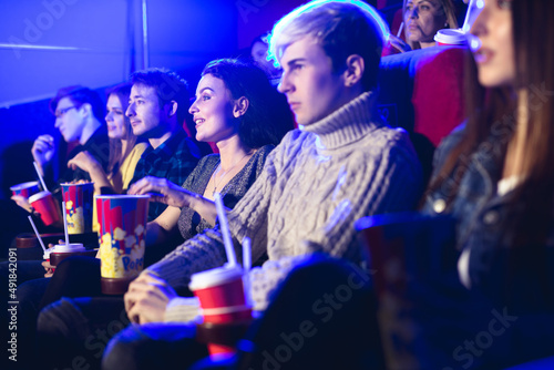 Friends sit and eat popcorn together while watching movies in a movie theater