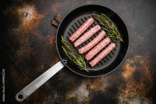 Raw sausage for frying, on frying cast iron pan, on old dark rustic table background, top view flat lay, with copy space for text