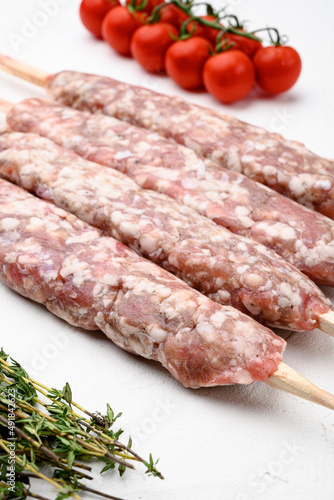 Minced and shaped lamb mutton kebabs, with grill ingredients, on white stone table background