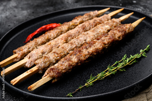 Minced and shaped lamb mutton kebabs, on plate, on black dark stone table background
