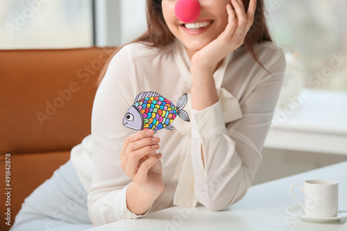 Young woman with clown nose and paper fish in office. April fools day celebration