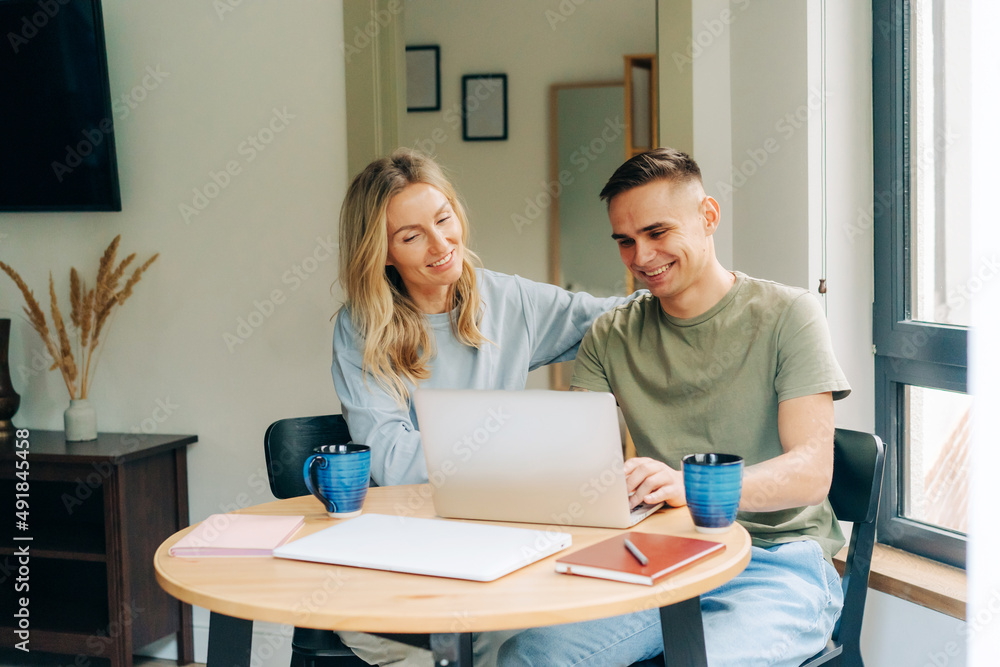 Young happy couple in love sitting home at the table, drinking coffee and working on the laptop. Young happy couple in love sitting home at the table, drinking coffee and working on the laptop.