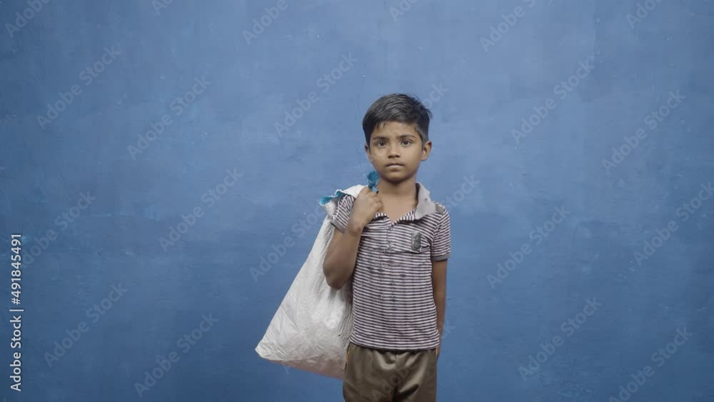 kid garbage walking into scene on blue background by looking at camera - concept of child labour, Poverty and rag picker kid garbage walking into scene on blue background by looking at camera - concept of child labour, Poverty and rag picker