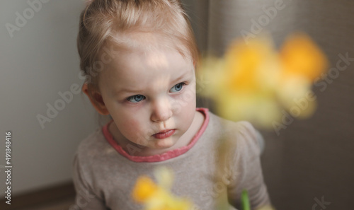 portrait of a little girl with yellow spring daffodil flower at home