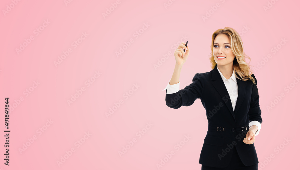 Smiling young businesswoman in black confident suit, writing or drawing on screen or transparent glass, by marker, isolated on pink background. Smiling young businesswoman in black confident suit, writing or drawing on screen or transparent glass, by marker, isolated on pink background.