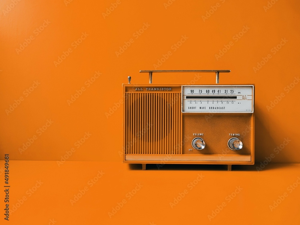Old transistor radio, orange wall background. Listen music concept - obrazy, fototapety, plakaty 