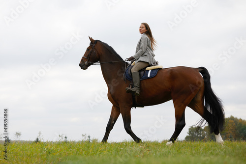 Beautiful young woman riding a horse on the field. Sideways to the camera. Freedom, joy, movement © Georgii
