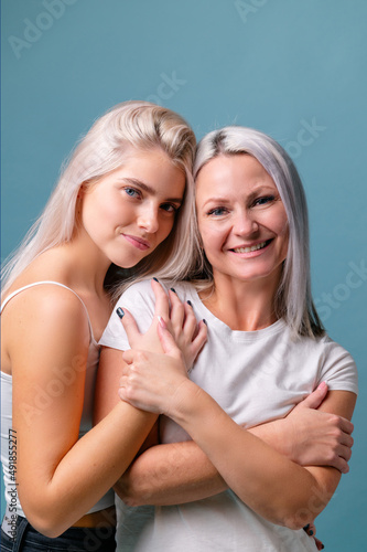 Blondehaired Mom and teenager daughter smiling on colorful backgroung. Middle studio shoot with copy space photo