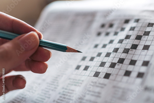 Close up hand holding pencil over crossword puzzle on newspaper. Game on for writing some letters to solve and completing the empty table. Focus on empty crossword table. photo